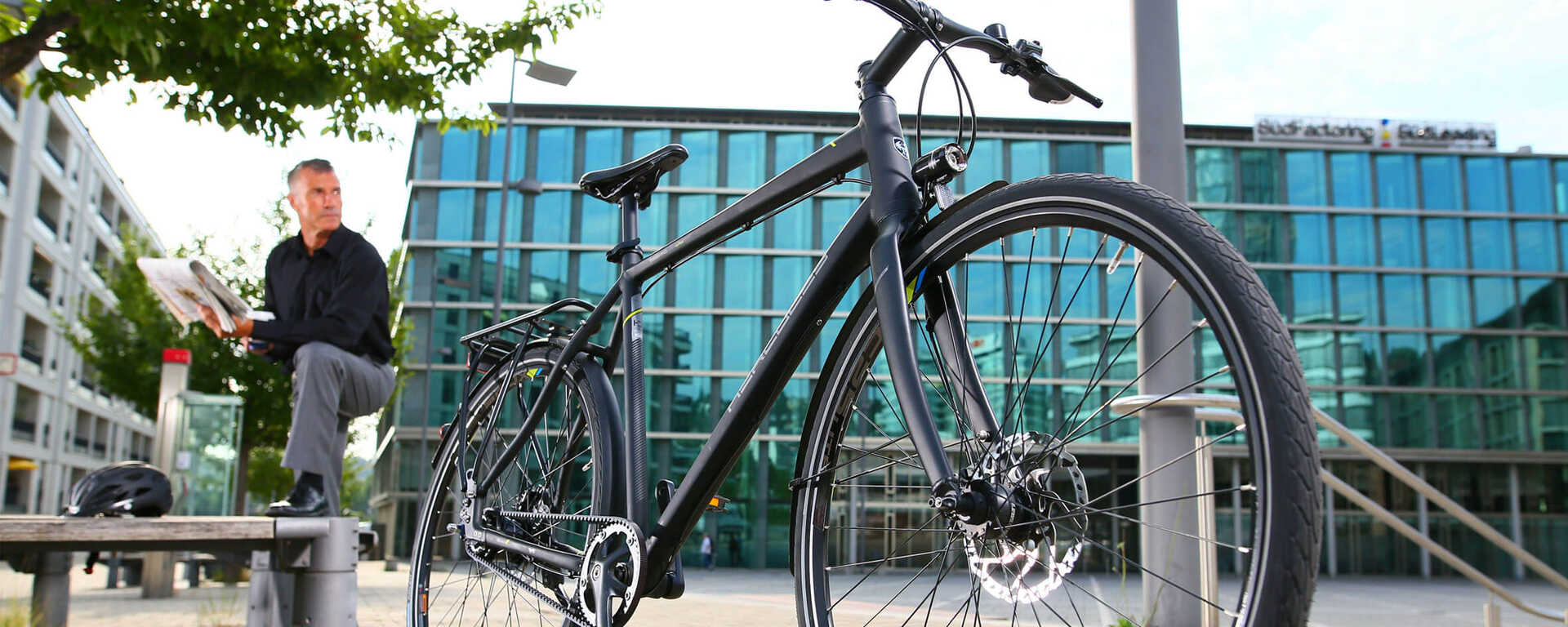 Fahrrad Kaufen Erlangen, Fürth, Nürnberg Fahrrad steht vor einem Gebäude. Im Hintergrund steht lessig ein Mann dersein Fahrrad anschaut.