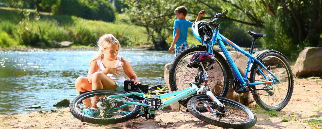 zwei Kinder sind mit Ihren Jugend & kinderfahrrädern an einem Fluss