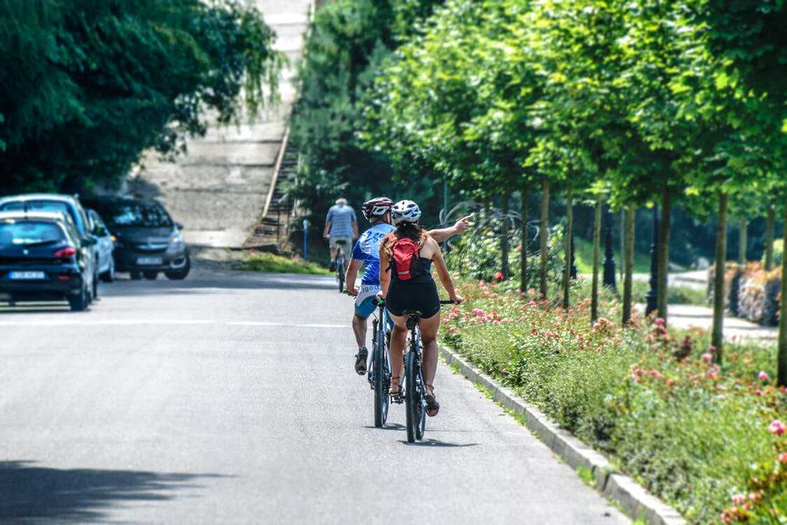 zwei Fahrradfahrer fahren mit Ihren Fahrrädern auf einer Strasse, rechts von Ihnen befinden sich Bäume