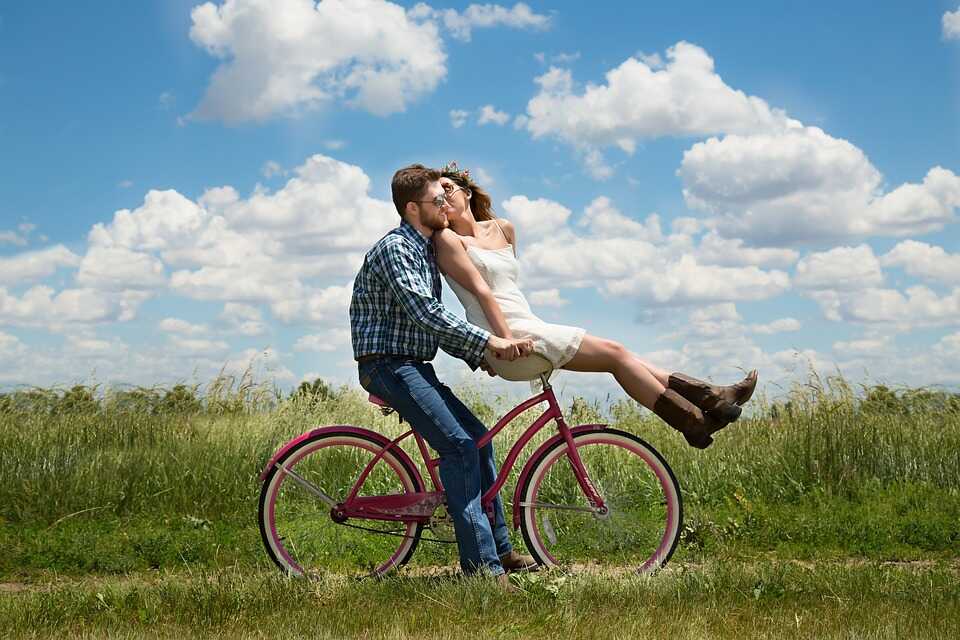 Ein Mann sitzt auf einem pinken Cityrad. Auf dessen Fahrrad Lenker sitzt eine Frau