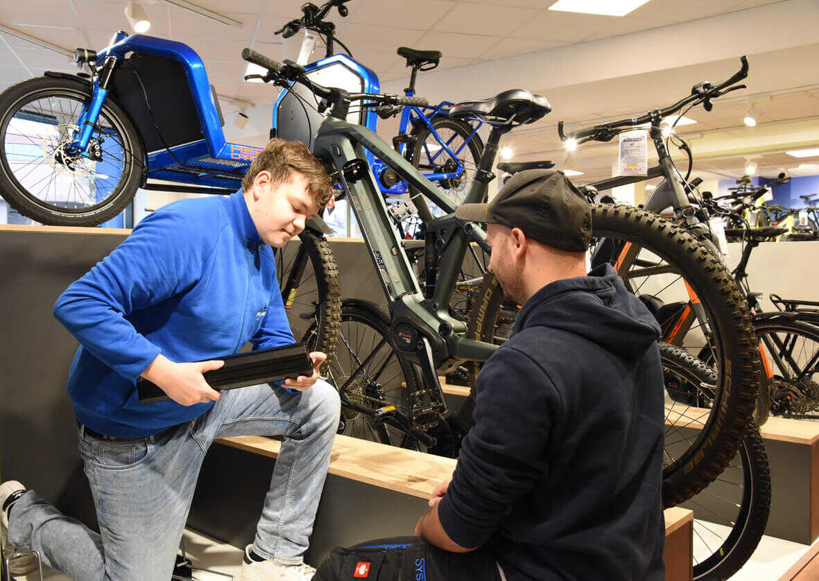 Azubi zeigt einem Kunden, wie man einen Bosch Akku aus einem E-Bike herausnimmt