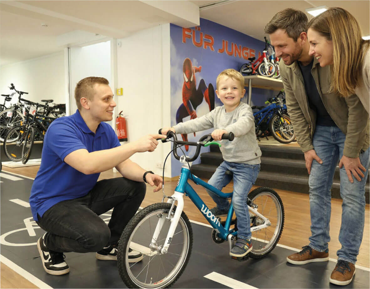Beratung im Bike Center Schreiber: Verkäufer berät Eltern und Kind am woom Kinderfahrrad